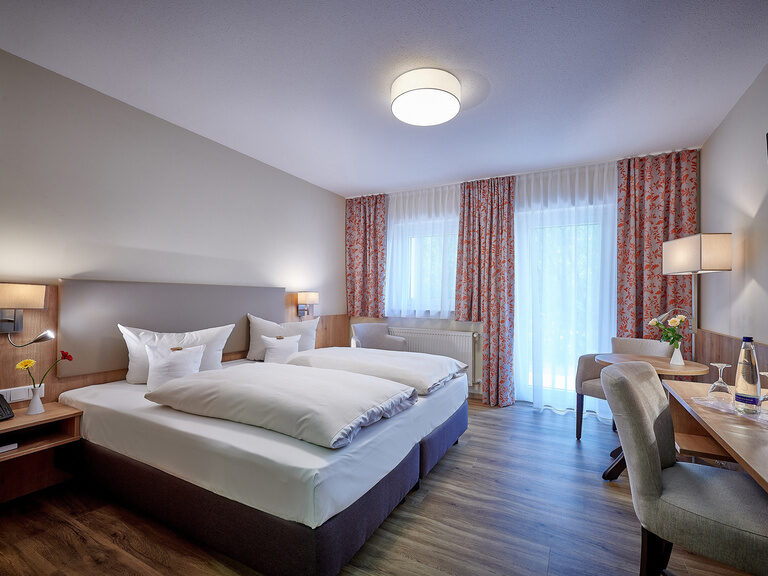 Ein Bett im Doppelzimmer Ahorn mit weicher Bettwäsche und einem stilvollen Fernseher an der Wand.